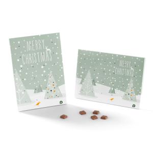 Two green Christmas cards with illustrated snowy trees and Merry Christmas text, displayed upright and flat, with small brown treats placed in front of them on a white background.